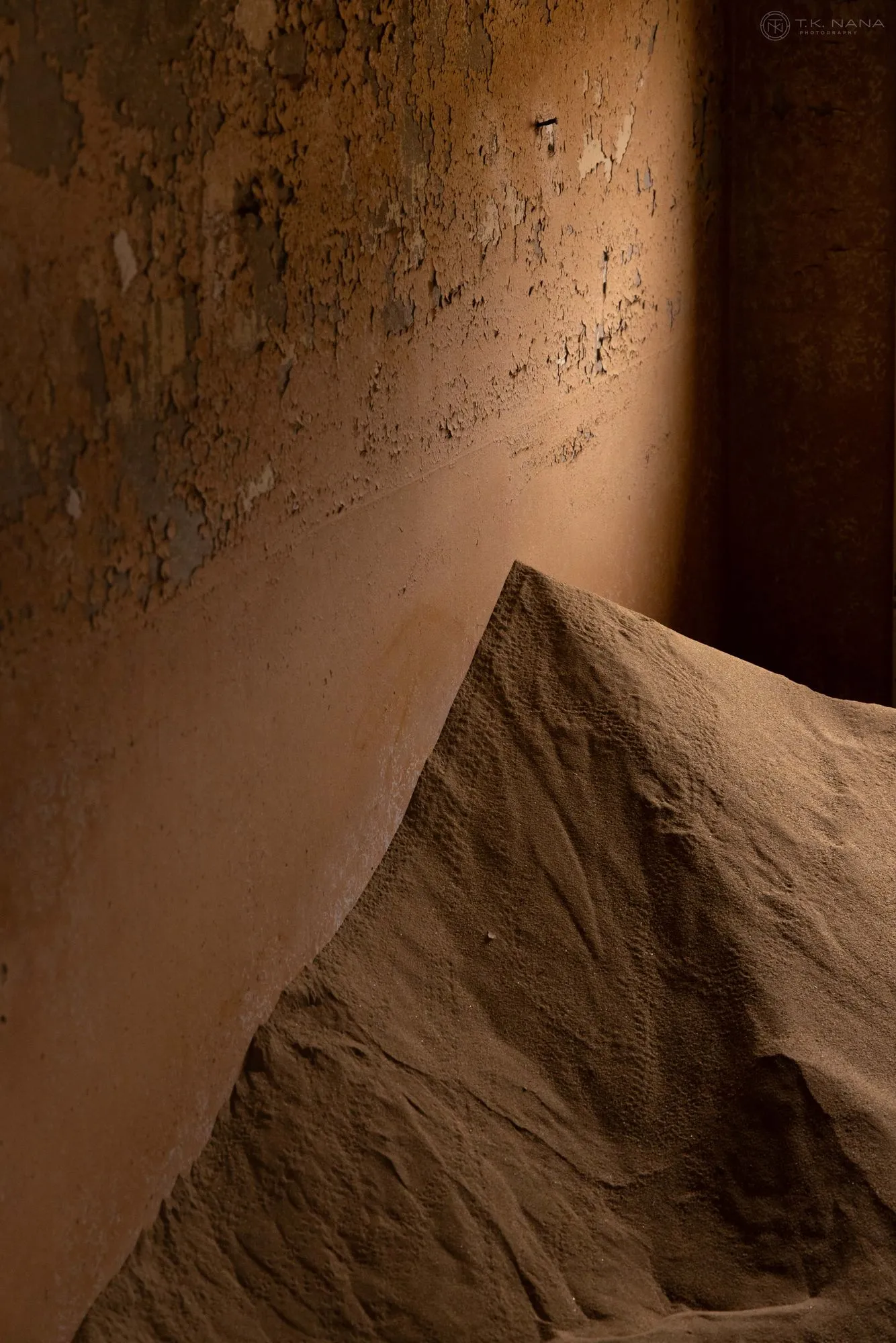 A dune of sand piled against a lamp-lit wall inside an abandoned house