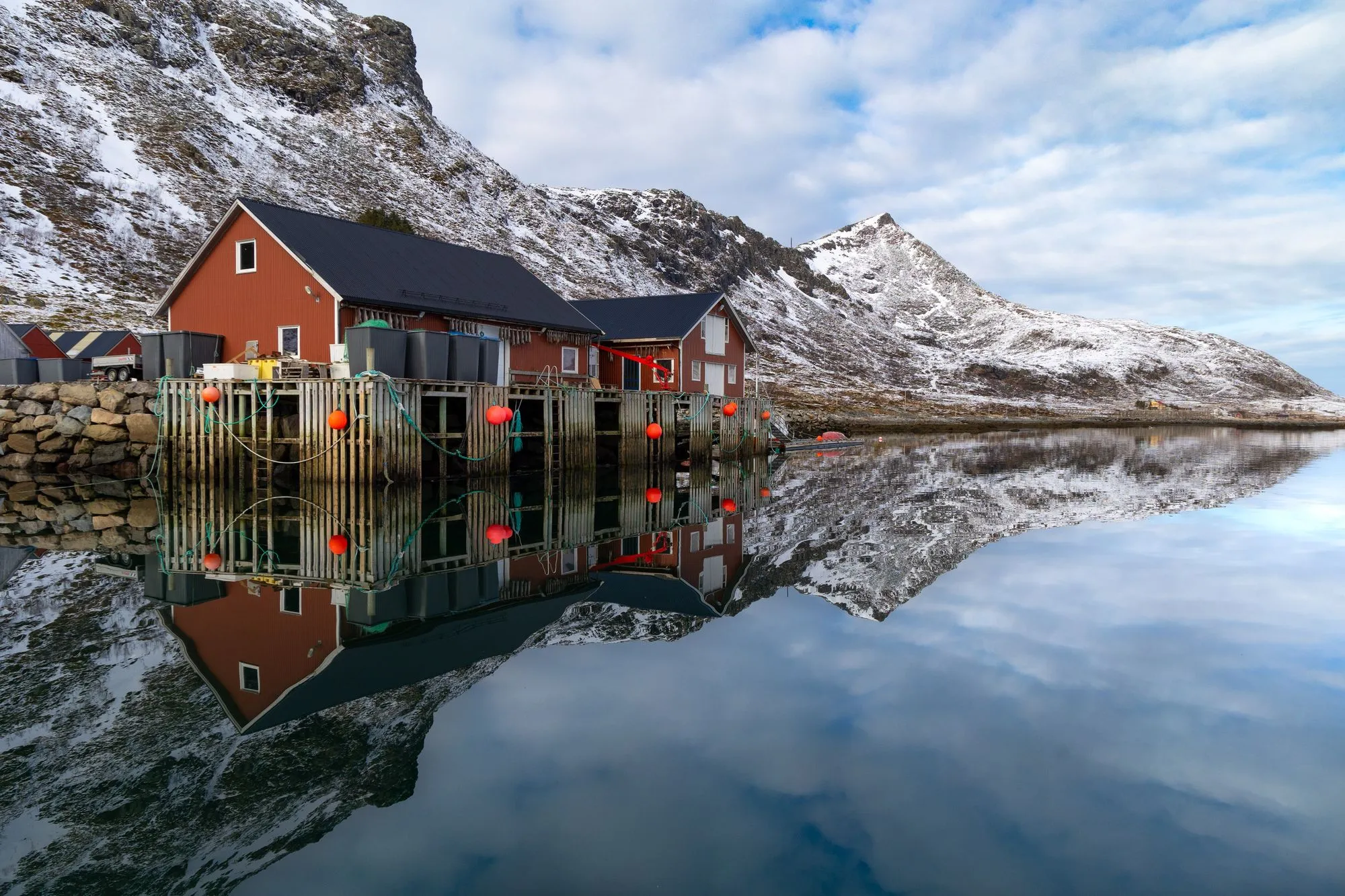Red fishing cabins and snowy peaks mirrored in a still fjord