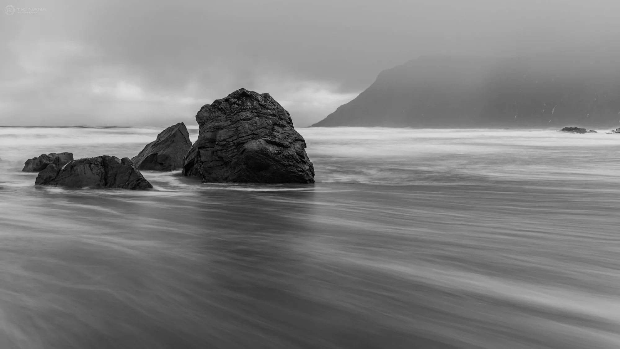 Long-exposure black-and-white of surf around rocks on a beach